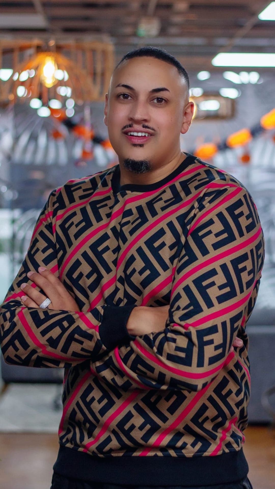 Kris Trinity standing with arms crossed, smiling, in a patterned sweater